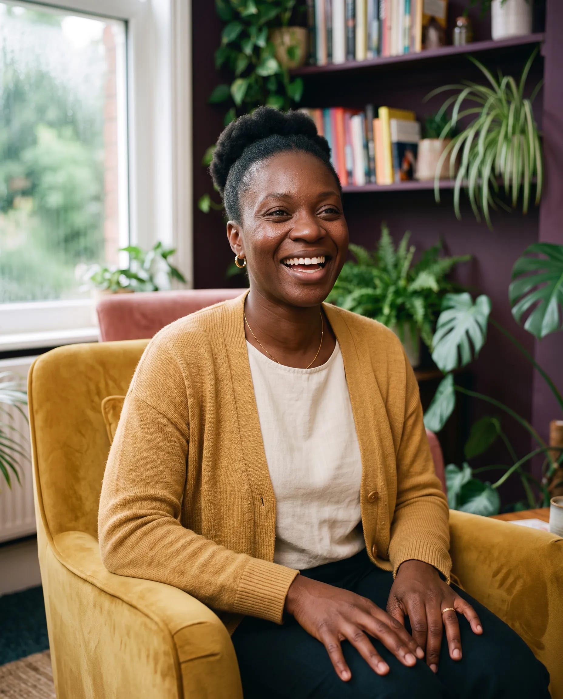 Afia Mensah, counsellor and psychotherapist, laughing warmly in her plant-filled therapy room in Birmingham